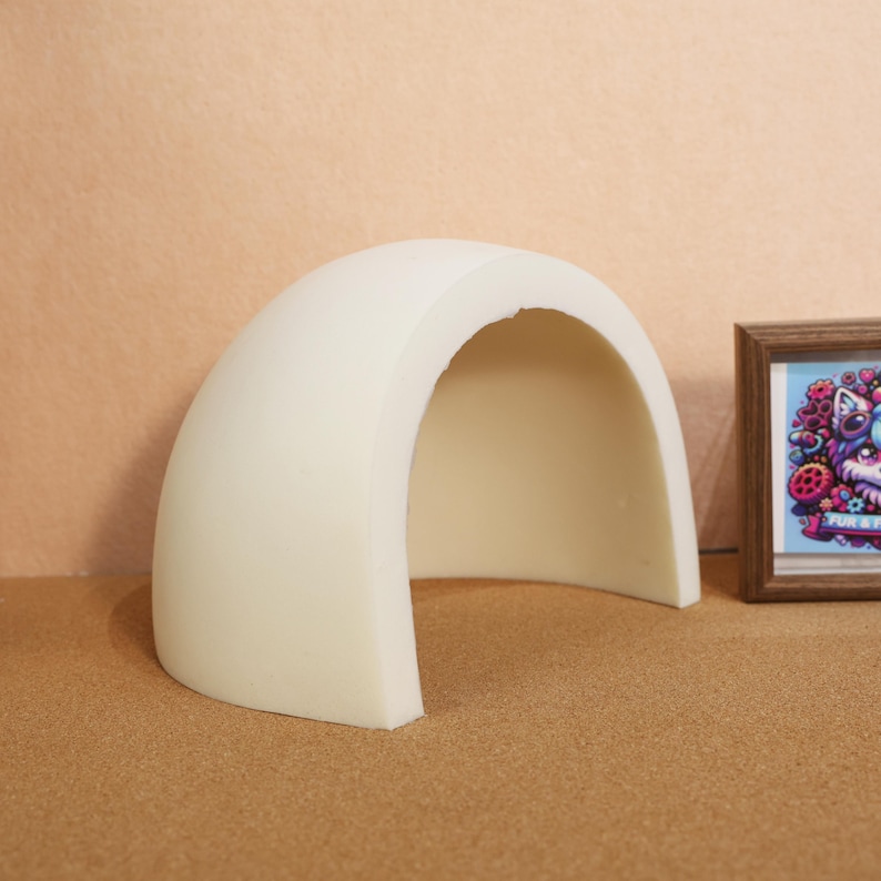 Pode incluir: Uma estrutura de arco semicircular em tom esbranqui&ccedil;ado, lisa e feita de material s&oacute;lido. O arco tem um interior oco e um perfil superior curvo. Ao lado do arco, encontra-se uma pequena moldura de madeira retangular com uma ilustra&ccedil;&atilde;o colorida.