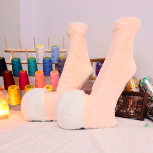 May include: Two pairs of fuzzy socks with a peach colored base and white fuzzy trim. The socks are laying on a white surface.