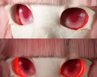 May include: Close-up of two sets of doll eyes. The eyes are a vibrant red with a white surrounding. The top set has a pinkish hue, while the bottom set glows with a bright red light. Pink wig hair frames the eyes.
