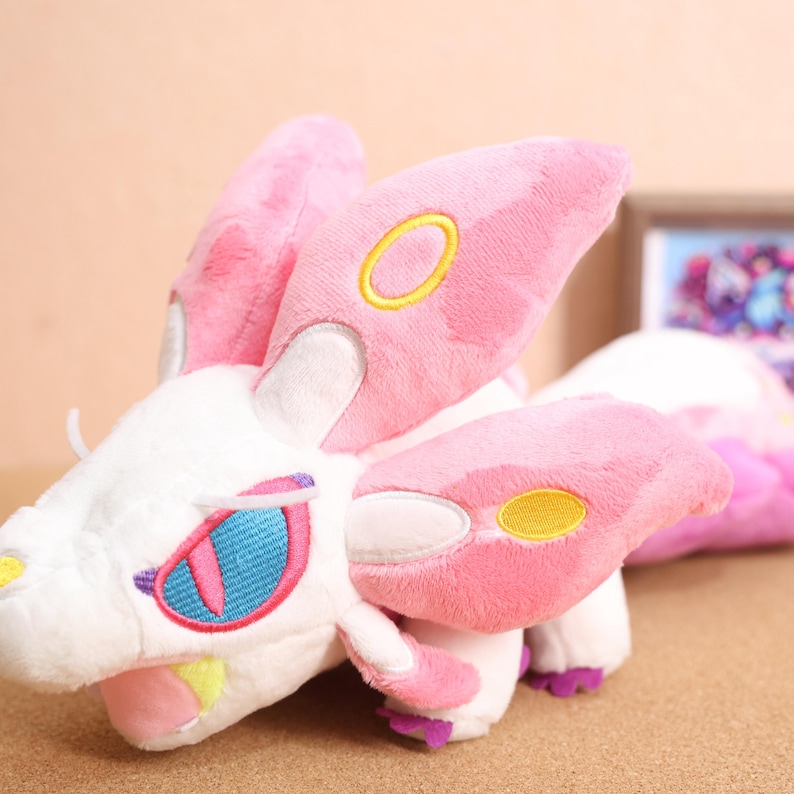 May include: Pink and white plush toy with yellow and blue embroidered details. The toy has a long tail and large ears.