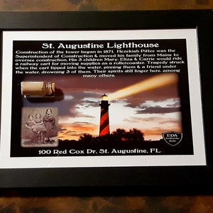 May include: Framed print of the St. Augustine Lighthouse with a black frame. The print includes a small vial, a sepia-toned photo of three girls, and text detailing the lighthouse's history and address.