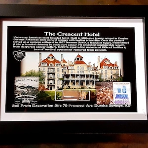 May include: A framed black and white photo of the Crescent Hotel in Eureka Springs, Arkansas. The photo is accompanied by text describing the hotel's history as a luxury retreat, women's college, and hospital. The text also mentions the hotel's reputation as one of America's most haunted hotels. The caption includes the text "Soil From Excavation Site 75 Prospect Ave, Eureka Springs, AR".