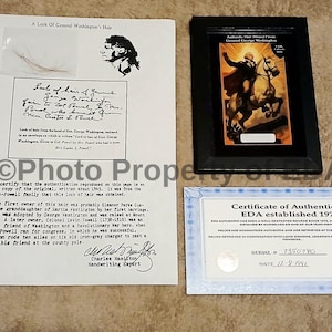 May include: An assortment of historical documents and artifacts, including a framed image of George Washington on horseback, a certificate of authenticity, and a document with a lock of hair and handwritten text.