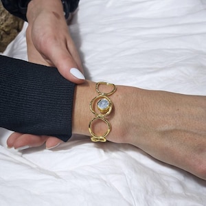 Pode incluir: Pulseira de ouro com um design circular e uma pedra branca no centro.