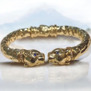May include: A gold bangle bracelet with two panther heads on the ends. The panther heads have blue eyes and are set with small diamonds.