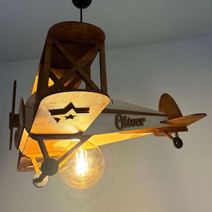 Natural wood airplane lamp glowing warmly – handmade wooden biplane nursery night light.