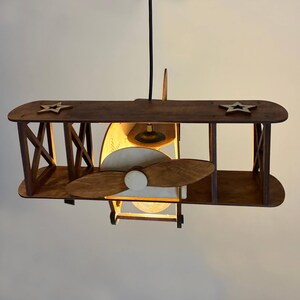 Natural wood biplane night light glowing warmly, handmade wooden airplane lamp for nursery decor