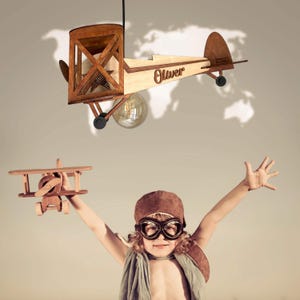 Happy boy dreaming of flying under a handmade wooden airplane lamp – Mood4Wood nursery decor.
