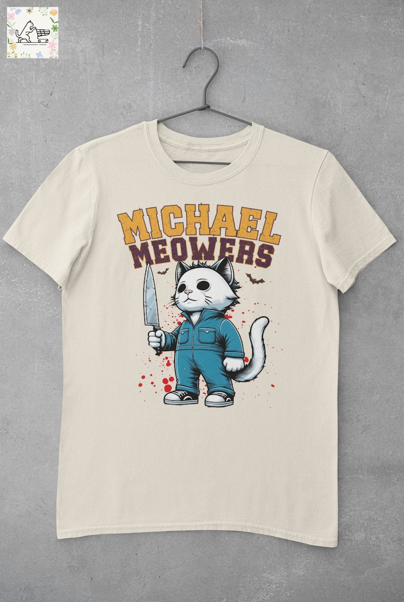 May include: A beige t-shirt with a graphic of a white cat holding a knife. The cat is wearing blue overalls and has a menacing expression. The text "MICHAEL MEOWERS" is printed in yellow above the cat.