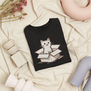 May include: Black t-shirt with a white cat in a box graphic. The cat is looking out of the box with a smile.
