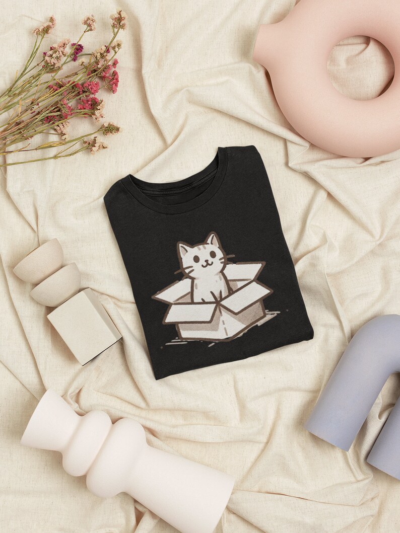 May include: Black t-shirt with a white cat in a box graphic. The cat is looking out of the box with a smile.