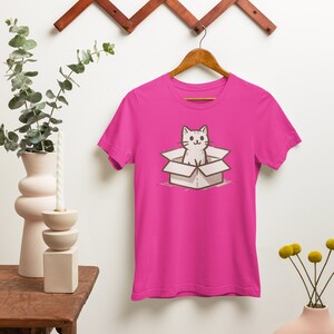 May include: A pink t-shirt with a cartoon illustration of a white cat sitting in a cardboard box.