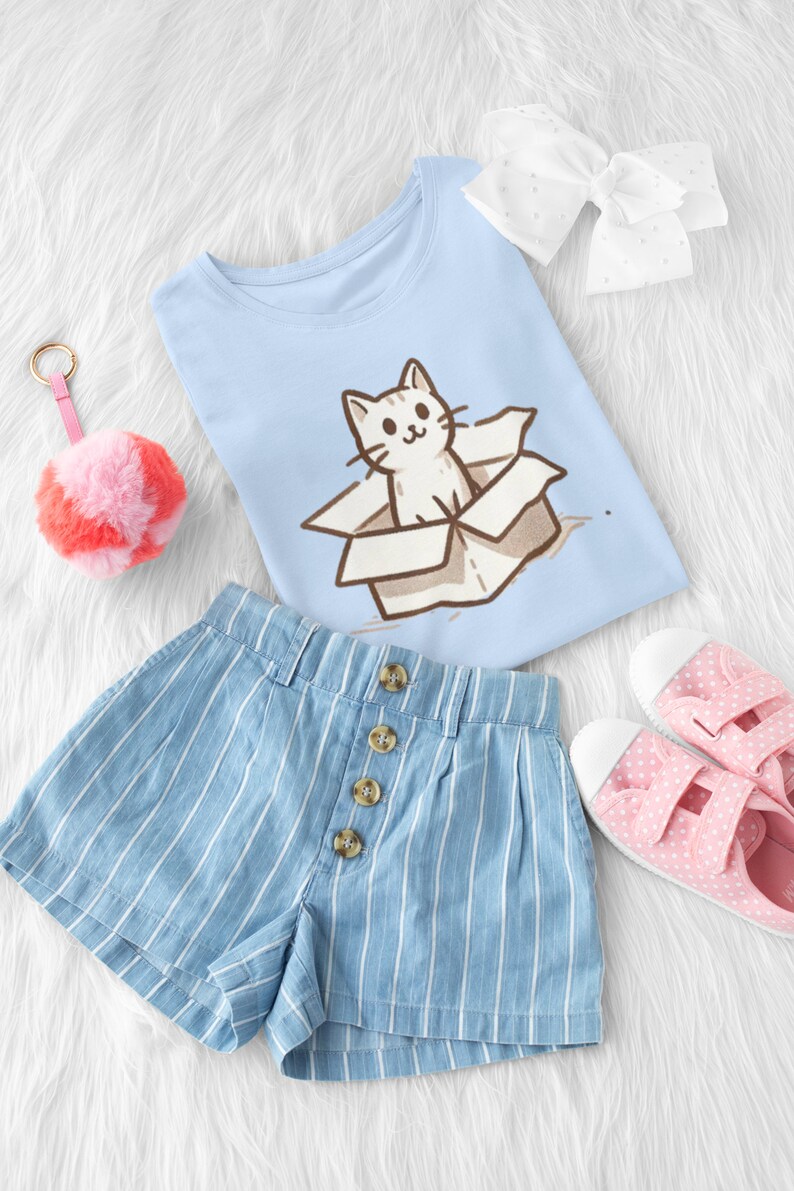 May include: A light blue t-shirt with a cartoon cat in a box graphic. The shirt is paired with blue and white striped denim shorts and pink polka dot canvas shoes.
