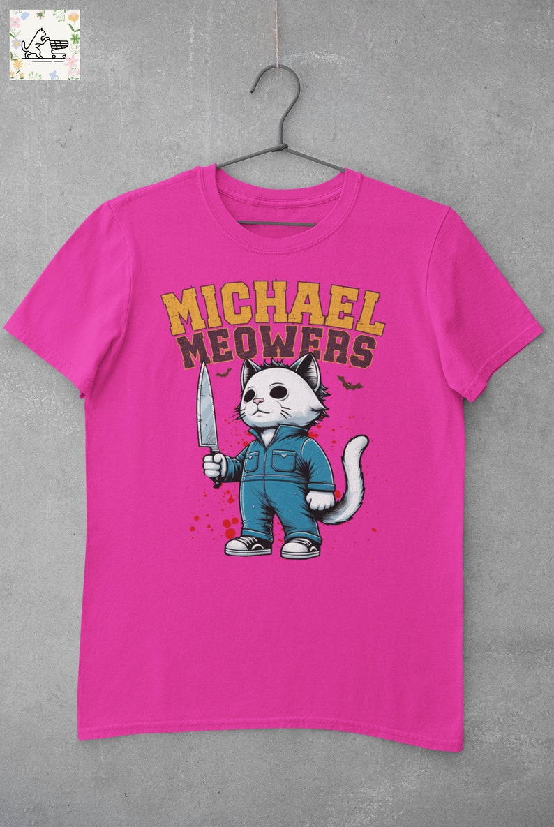 May include: A pink t-shirt with a graphic of a white cat holding a knife. The cat is wearing blue overalls and has a white tail. The text "MICHAEL MEOWERS" is printed in yellow above the cat.
