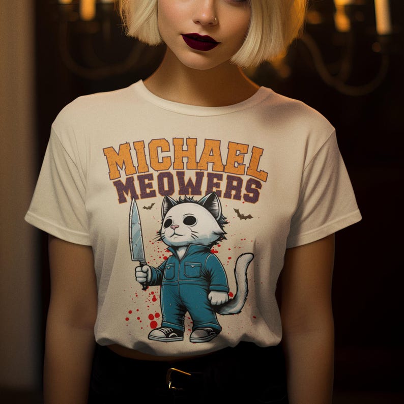 May include: White t-shirt with a graphic of a cat holding a knife. The text "MICHAEL MEOWERS" is printed above the cat.