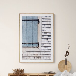Può includere: Una fotografia incorniciata di una porta in legno blu con rivestimento in legno bianco. La foto è appesa a una parete bianca sopra un letto bianco con biancheria da letto blu.