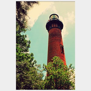 May include: A red brick lighthouse with a black roof and a white lantern room. The lighthouse is surrounded by green trees and a blue sky with white clouds.