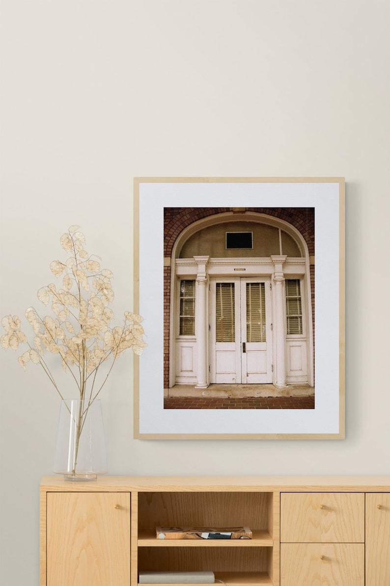 May include: A framed photograph of a white double door with a brick archway above. The door has a transom window and is surrounded by white columns.