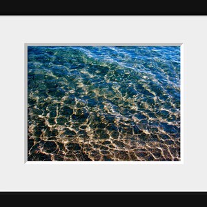 Pu&ograve; includere: Una foto ravvicinata del fondo di un corpo d'acqua. L'acqua &egrave; limpida e si pu&ograve; vedere il fondo sabbioso attraverso l'acqua. L'acqua &egrave; di colore blu chiaro e la sabbia &egrave; di colore marrone chiaro.