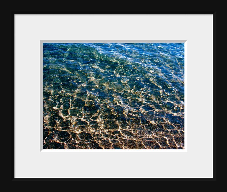 Pu&ograve; includere: Una foto ravvicinata del fondo di un corpo d'acqua. L'acqua &egrave; limpida e si pu&ograve; vedere il fondo sabbioso attraverso l'acqua. L'acqua &egrave; di colore blu chiaro e la sabbia &egrave; di colore marrone chiaro.