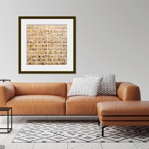 May include: A framed photograph of a wall filled with small, colorful jars. The jars are arranged in a grid pattern and are filled with various objects, such as buttons, beads, and other small trinkets. The photograph is hanging on a white wall in a living room setting.