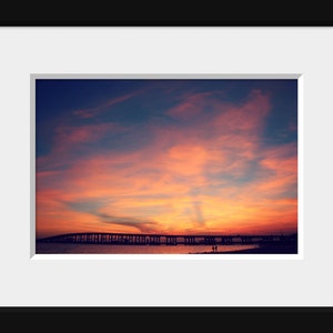 May include: A scenic photograph of a bridge silhouetted against a vibrant sunset sky. The sky is a mix of pink, orange, and purple hues, creating a dramatic backdrop for the bridge.