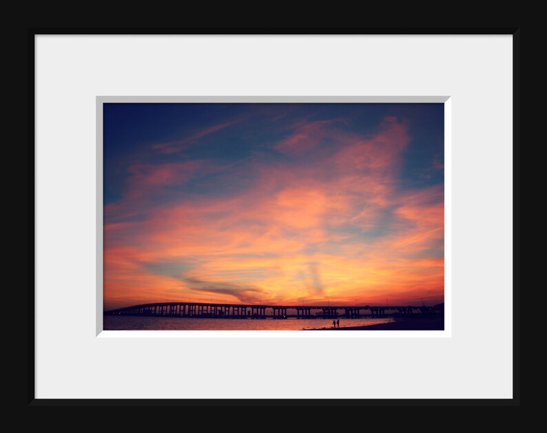 May include: A scenic photograph of a bridge silhouetted against a vibrant sunset sky. The sky is a mix of pink, orange, and purple hues, creating a dramatic backdrop for the bridge.