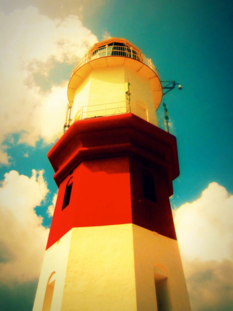 May include: A red and white lighthouse with a white railing and a glass lantern on top. The lighthouse is against a blue sky with white clouds.