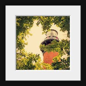 May include: A red brick lighthouse with a white railing and a glass top. The lighthouse is surrounded by green trees.
