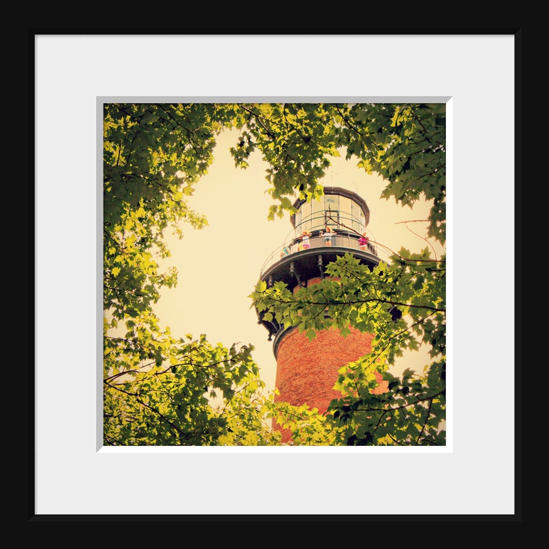 May include: A red brick lighthouse with a white railing and a glass top. The lighthouse is surrounded by green trees.
