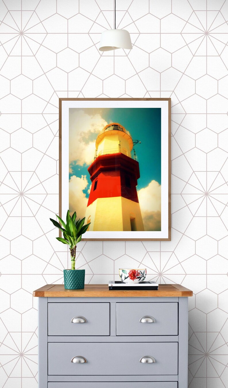 May include: A gray dresser with four drawers and wooden top. A framed picture of a red and white lighthouse against a blue sky is above the dresser. A small green plant and a bowl with red flowers are on the dresser.