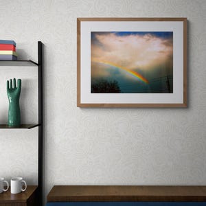 May include: A framed photograph of a rainbow appearing in a cloudy sky. The rainbow is bright and colourful, with red, orange, yellow, green, blue, indigo, and violet hues. The sky is a light blue, with white clouds.