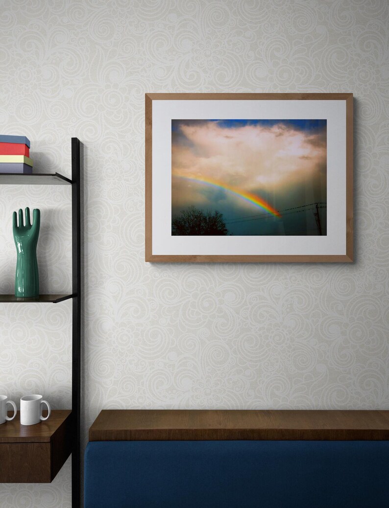 May include: A framed photograph of a rainbow appearing in a cloudy sky. The rainbow is bright and colourful, with red, orange, yellow, green, blue, indigo, and violet hues. The sky is a light blue, with white clouds.