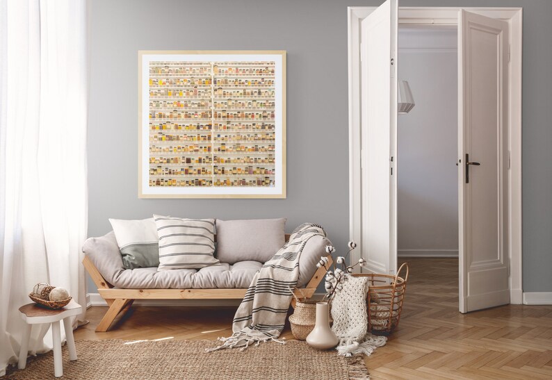 May include: A light gray living room with a wooden futon, a white stool, and a framed print of a wall of small jars filled with colorful spices. The futon has a white and gray striped throw blanket and two pillows. A wicker basket with a white knitted throw is on the floor next to the futon.