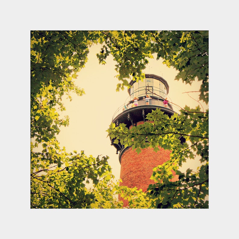 May include: A red brick lighthouse with a white railing and a green metal roof. The lighthouse is surrounded by green trees.