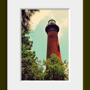 May include: A red brick lighthouse with a black roof and a white window stands tall against a blue sky with white clouds. Green trees surround the base of the lighthouse.