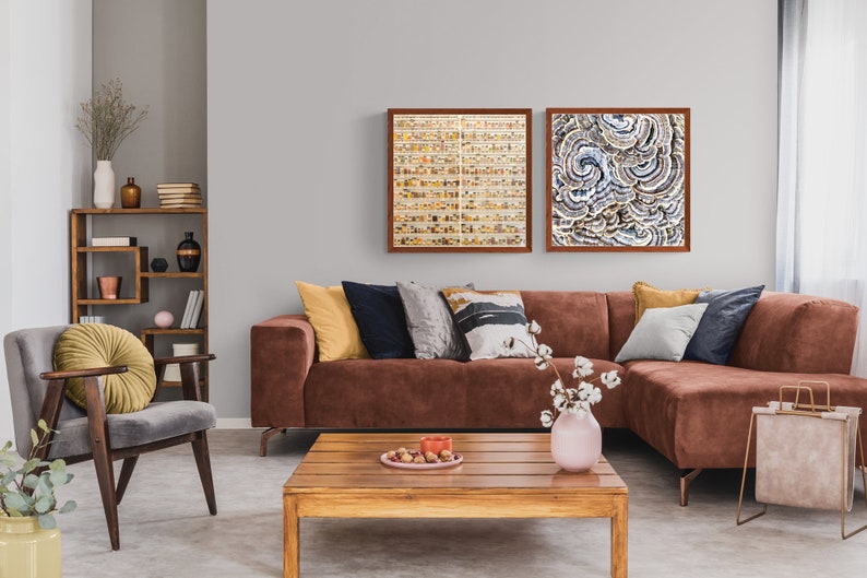 May include: A brown sectional sofa with yellow, blue, and gray throw pillows in a living room with a wooden coffee table, a gray armchair with a yellow pillow, and two framed abstract art prints on the wall.