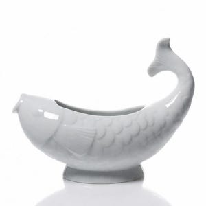 Peut inclure: Un plat de service en forme de poisson en céramique blanche. Le plat a un corps incurvé avec des détails d'écailles, une nageoire et une queue qui se courbe vers le haut. Il repose sur une petite base ronde. L'intérieur est ouvert pour servir.
