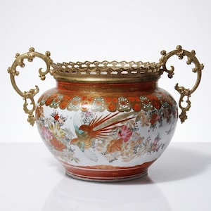 Peut inclure: Un vase décoratif en céramique avec un corps large et arrondi et des poignées en laiton ornées. Le vase présente un motif floral et aviaire vibrant en rouge, orange et blanc. Une bordure en filigrane en laiton orne le dessus.