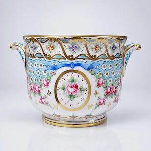 Peut inclure: Un cache-pot en porcelaine blanche orné de roses roses peintes à la main, de rubans bleus et de dorures. Le récipient possède deux anses latérales et un motif décoratif de petites fleurs et de points sur le bord et le corps.