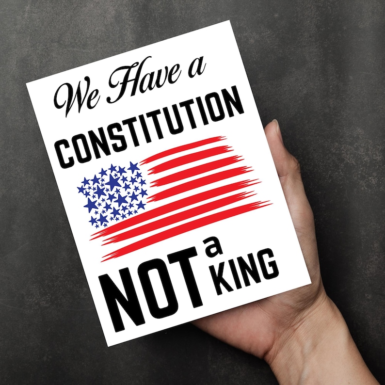 May include: A white card with the text "We Have a CONSTITUTION NOT a KING" in black script and bold font. The card features a stylized American flag with red stripes and blue stars.