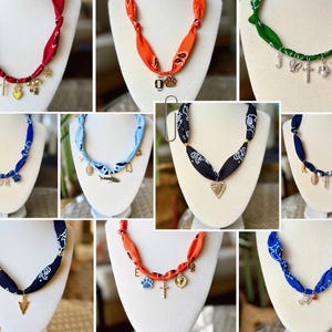 May include: A collection of nine necklaces made from rolled fabric bandanas in various colors including red, orange, green, blue, light blue, and black. Each necklace features a unique assortment of metal charms hanging from the fabric band.
