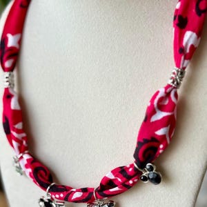 May include: A red fabric necklace with a white and black pattern. The necklace has silver accents and charms, including a Mickey and Minnie Mouse design and the word "love".
