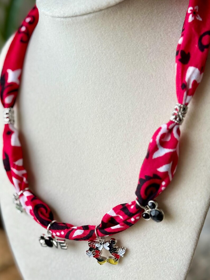 May include: A red fabric necklace with a white and black pattern. The necklace has silver accents and charms, including a Mickey and Minnie Mouse design and the word "love".