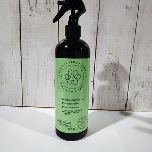 May include: A black spray bottle with a green label. The label reads "Bennett Family Farms Flea & Tick Spray" with a paw print design. It also states "Refreshing Cedarwood Scent." The bottle contains 473 ml.