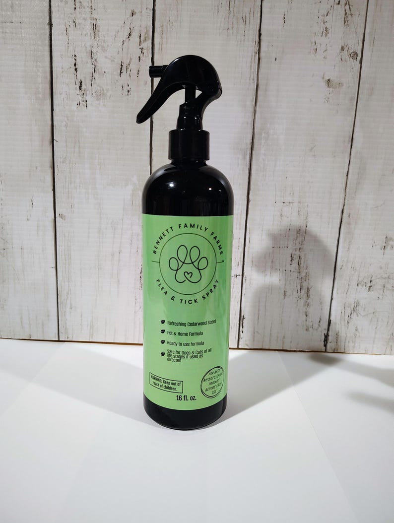May include: A black spray bottle with a green label. The label reads "Bennett Family Farms Flea & Tick Spray" with a paw print design. It also states "Refreshing Cedarwood Scent." The bottle contains 473 ml.