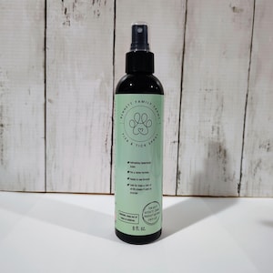 May include: A black spray bottle with a green label. The label reads "BENNETT FAMILY FARMS FLEA & TICK SPRAY" and features a paw print logo. It also states "Refreshing Cedarwood Scent". The bottle contains 237 ml.