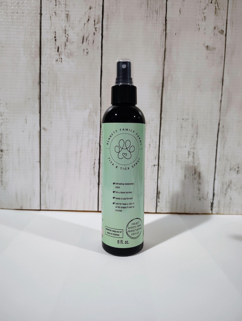 May include: A black spray bottle with a green label. The label reads "BENNETT FAMILY FARMS FLEA & TICK SPRAY" and features a paw print logo. It also states "Refreshing Cedarwood Scent". The bottle contains 237 ml.