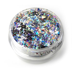 May include: A clear, round container filled with iridescent glitter flakes. The glitter reflects a spectrum of colors, including silver, blue, green, and purple. The container has the text "JetNge Studio" printed on the side.