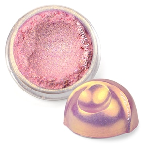Può includere: Un barattolo rotondo in plastica trasparente riempito con polvere cosmetica rosa scintillante con sottotoni dorati. Accanto al barattolo si trova un coperchio abbinato, iridescente e a cupola con finitura metallica. Il testo Jeung Studio è stampato su entrambi.